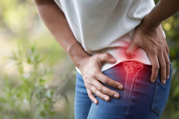 A woman is holding her hip, expressing pain, with a red overlay that highlights the area of discomfort. This image visually represents common hip injuries and conditions such as arthritis and bursitis.