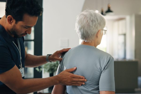 Old woman, chiropractor and back exam in nursing home with support, wellness and rehabilitation. Senior person, orthopedic worker and help in retirement center for spine injury, healing and recovery